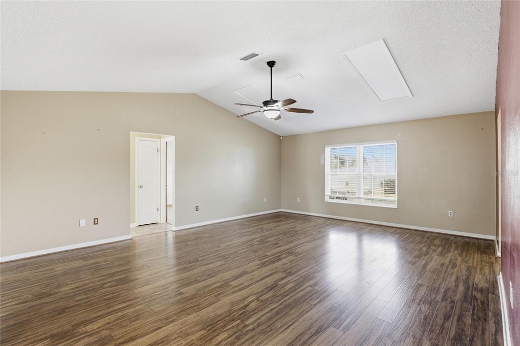 An empty living room features vaulted ceilings, a ceiling fan, and wood-look laminate flooring — 3940 SW 134TH STREET, OCALA, FL