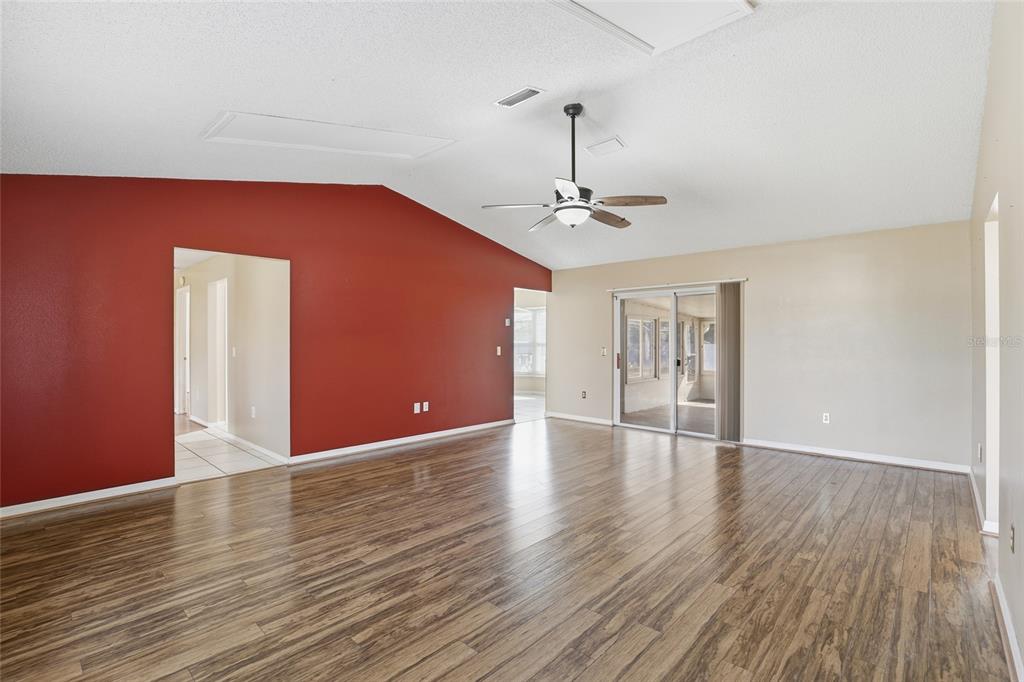 A living room with wood-look flooring, a vaulted ceiling, a ceiling fan, and red walls — 3940 SW 134TH STREET, OCALA, FL