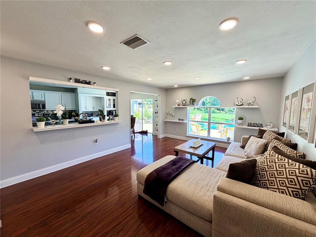 A living room features dark hardwood floors, a sectional sofa, and a pass-through to the kitchen — 30341 PONGO WAY, WESLEY CHAPEL, FL