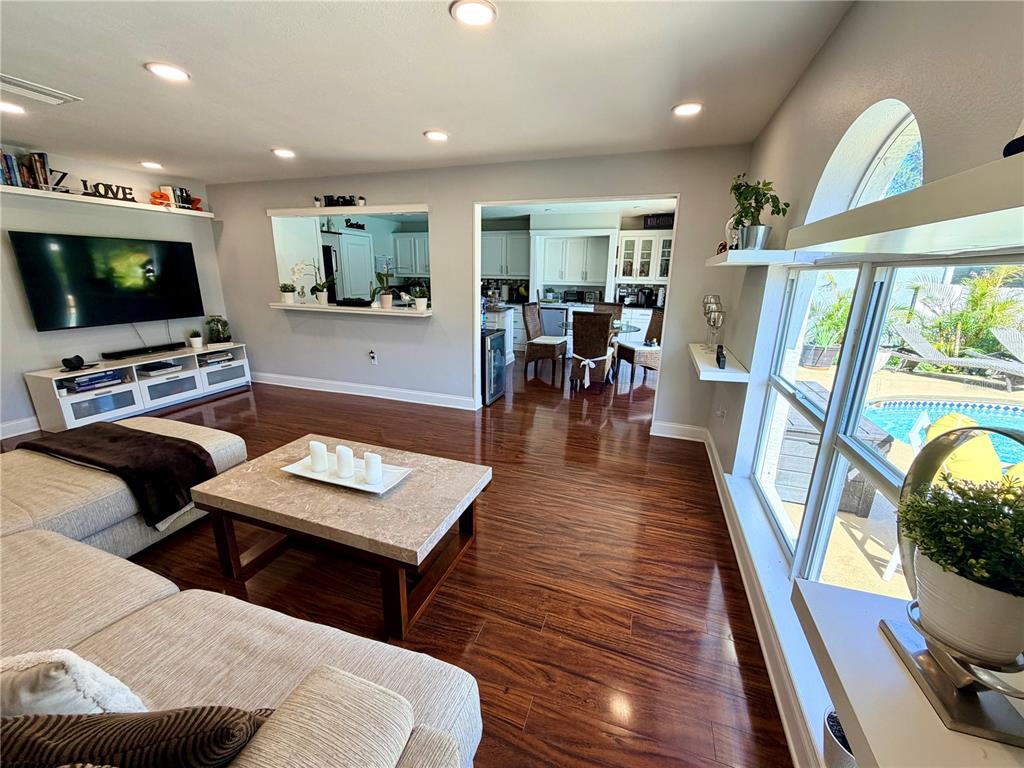 A living room with hardwood floors, a large television, and a view of a pool — 30341 PONGO WAY, WESLEY CHAPEL, FL