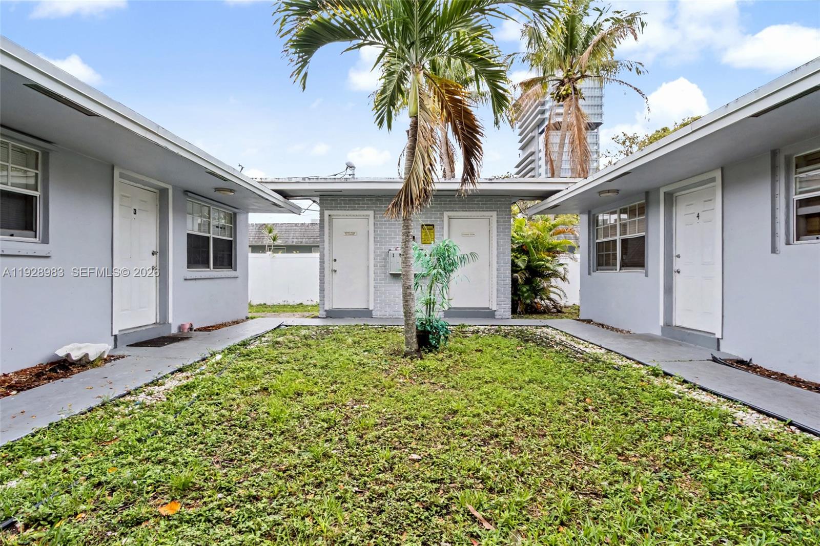 A courtyard with a palm tree sits between two gray buildings with numbered doors — 923 SE 2nd Ave # 6, Hallandale Beach FL 33009, HALLANDALE BEACH, FL
