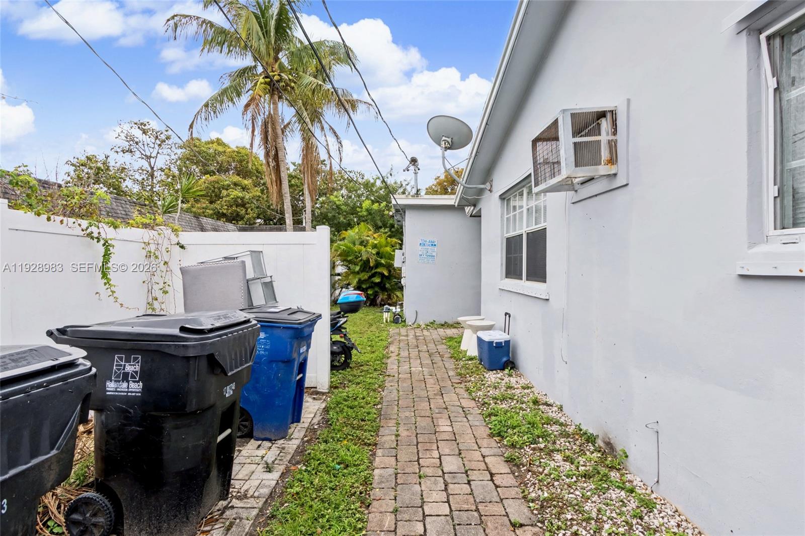 A paved walkway leads along the side of a house with trash bins and vegetation — 923 SE 2nd Ave # 6, Hallandale Beach FL 33009, HALLANDALE BEACH, FL
