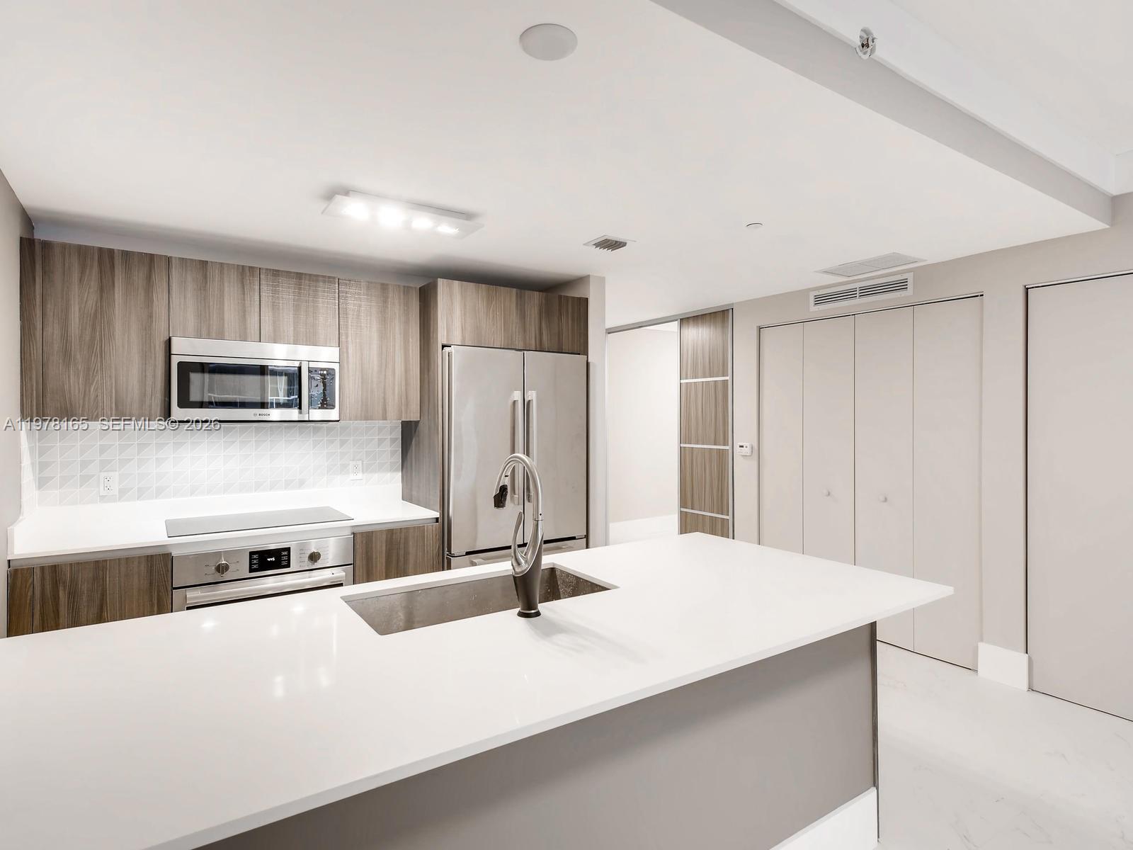 A modern kitchen features wood-grain cabinets, stainless steel appliances, and a white quartz island countertop — 488 NE 18th St # 2507, Miami FL 33132, MIAMI, FL