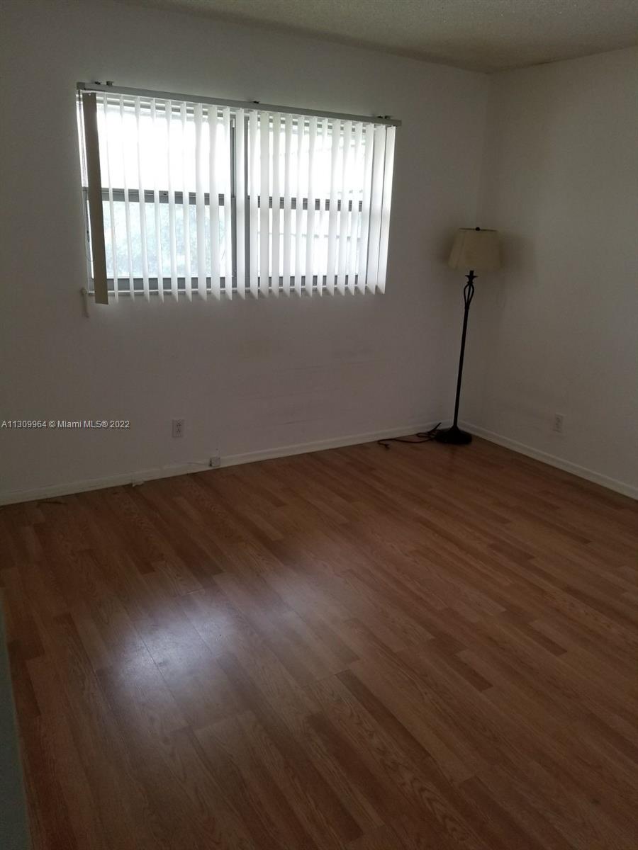 An empty room features light wood-look flooring, white walls, vertical blinds, and a floor lamp — 5790 Stirling Rd # 314, Hollywood FL 33021, HOLLYWOOD, FL