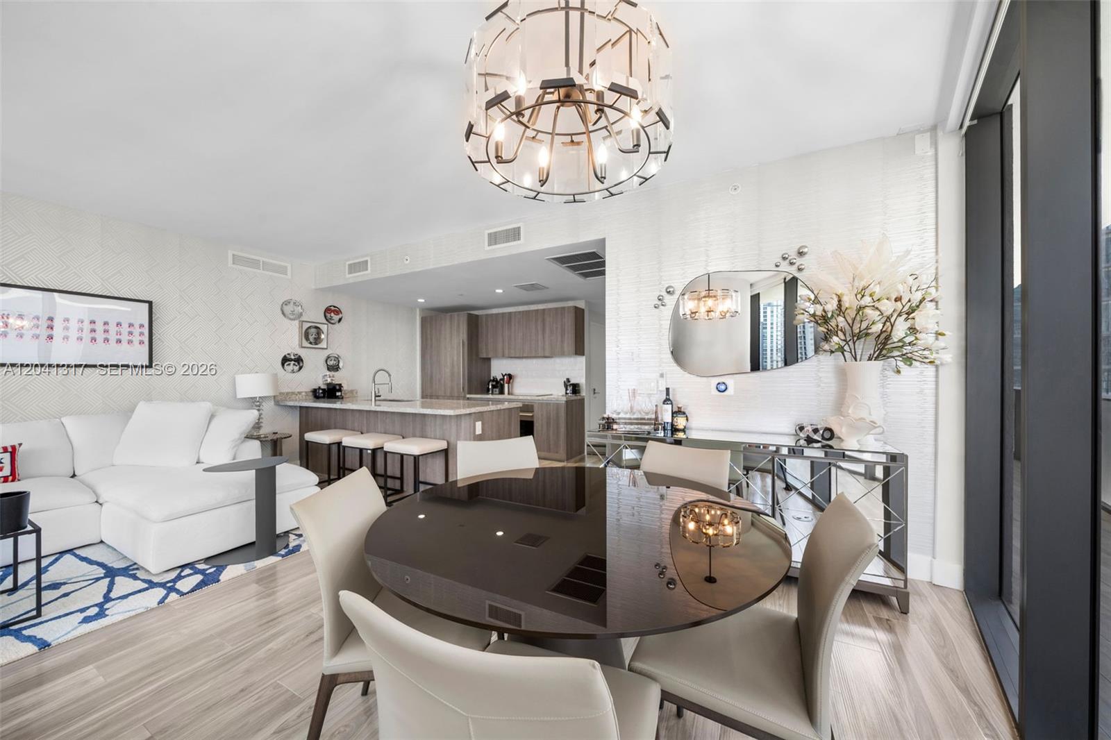 A modern open-concept living and dining area features a round table, chandelier, and kitchen island — 801 S Miami Ave # 1604, Miami FL 33130, MIAMI, FL