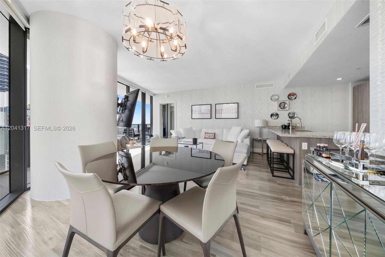 A modern dining and living area features a glass table, chandelier, and open kitchen — 801 S Miami Ave # 1604, Miami FL 33130, MIAMI, FL