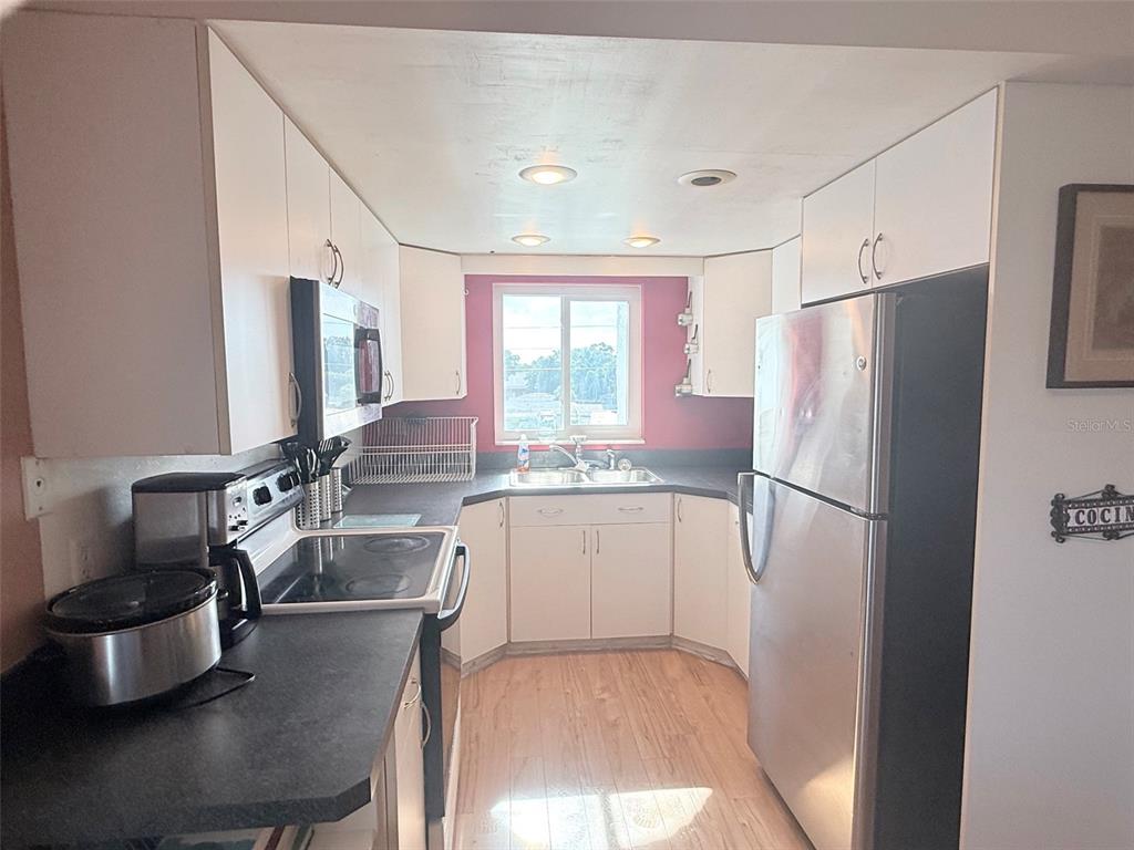 A galley kitchen features white cabinets, stainless steel appliances, dark countertops, and a window — 1200 37TH STREET N UNIT 409, ST PETERSBURG, FL