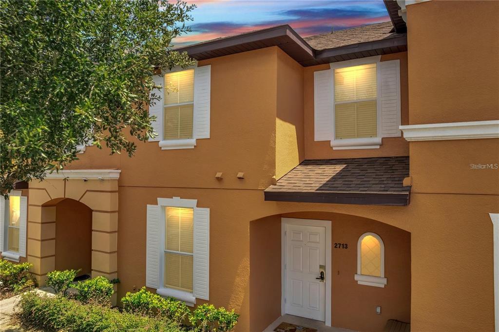 A two-story townhouse exterior features orange stucco walls, white window shutters, and a front door — 2713 BUSHMAN DRIVE, KISSIMMEE, FL