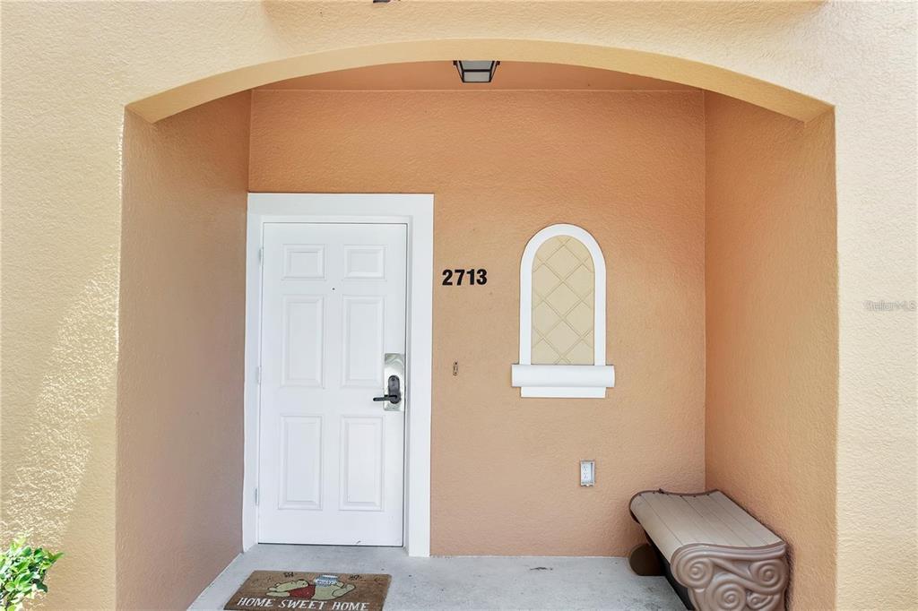 A covered entryway features a white door, a small bench, and a decorative wall niche — 2713 BUSHMAN DRIVE, KISSIMMEE, FL