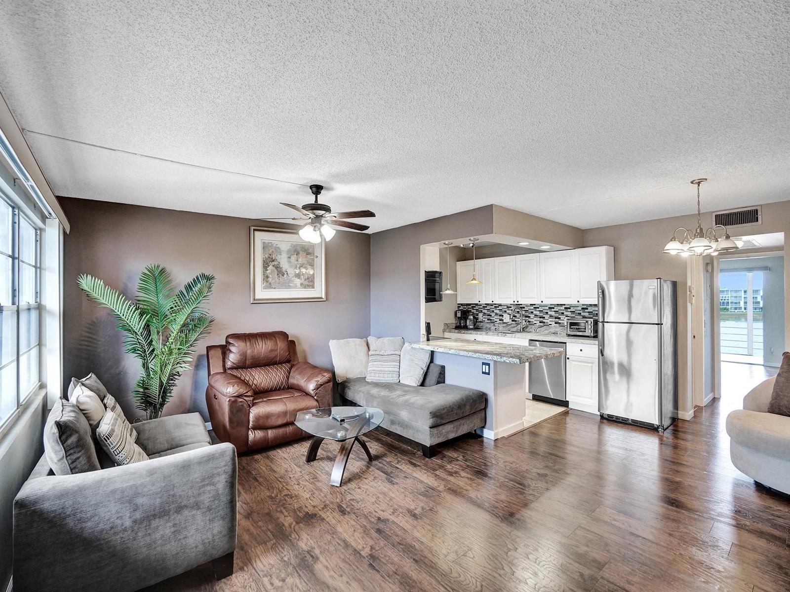 An open-concept living room and kitchen featuring wood flooring, a ceiling fan, and stainless appliances — 3014 Cornwall A, Boca Raton FL 33434, BOCA RATON, FL