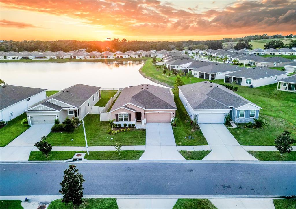 A grassy backyard features a white vinyl fence overlooking a pond at sunset — 8349 WHEAT STONE DRIVE, ZEPHYRHILLS, FL