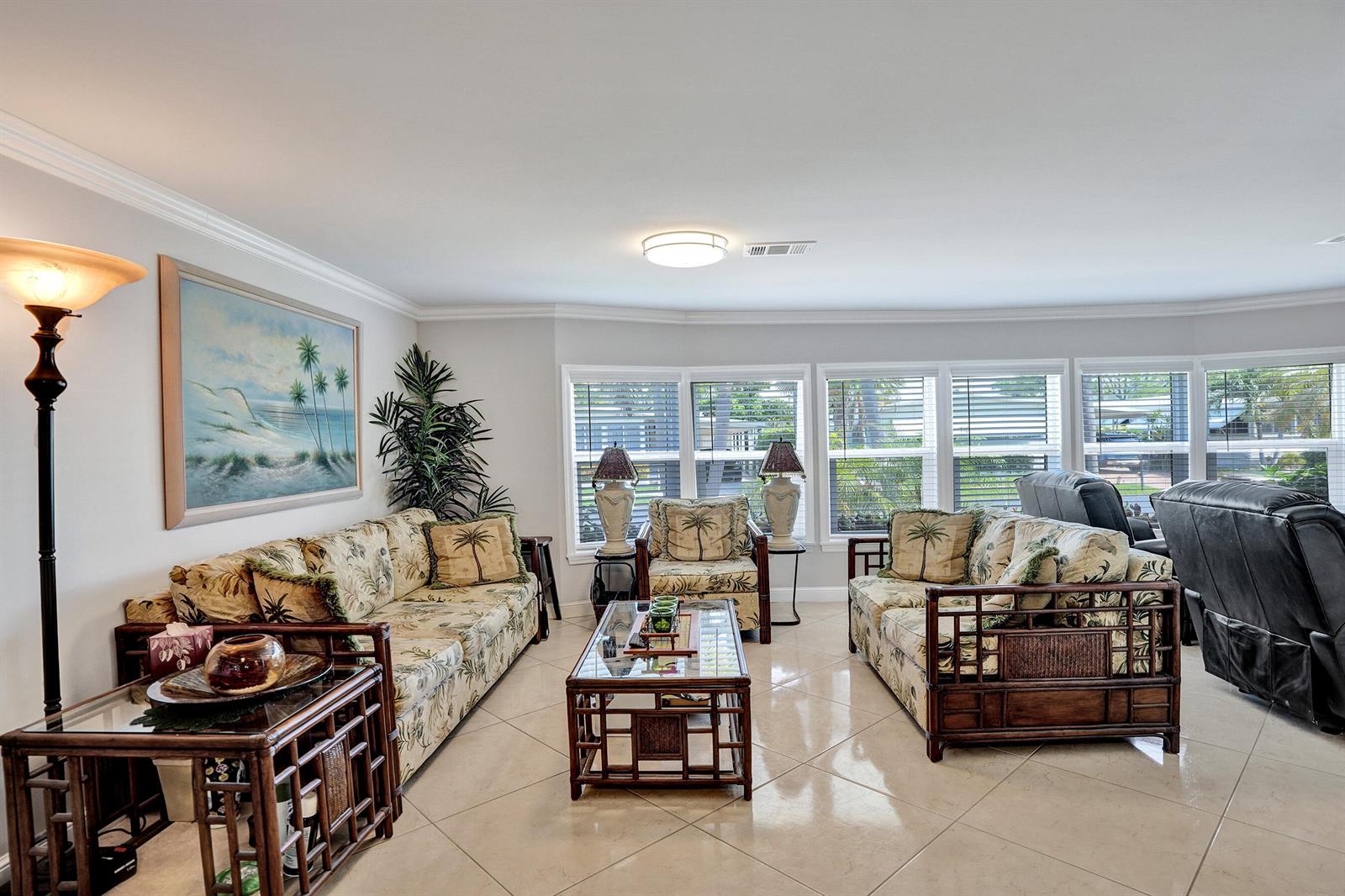 A living room features rattan furniture, palm-print cushions, tile flooring, and large windows — 120 NW 53rd Place, Pompano Beach FL 33064, POMPANO BEACH, FL