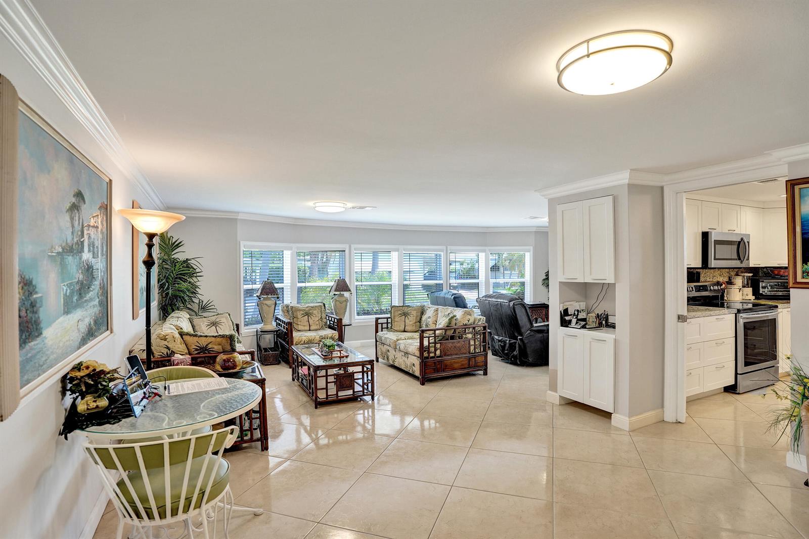 A bright living room with tile floors, tropical-patterned furniture, and an adjacent white kitchen — 120 NW 53rd Place, Pompano Beach FL 33064, POMPANO BEACH, FL