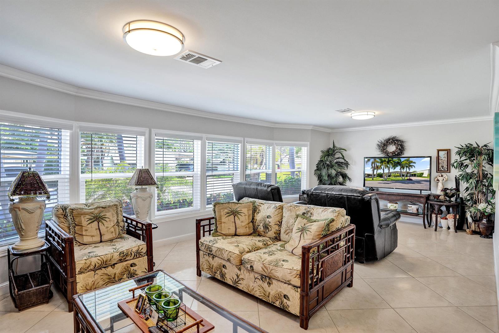 A living room features tropical-patterned furniture, tile flooring, and large windows with white blinds — 120 NW 53rd Place, Pompano Beach FL 33064, POMPANO BEACH, FL