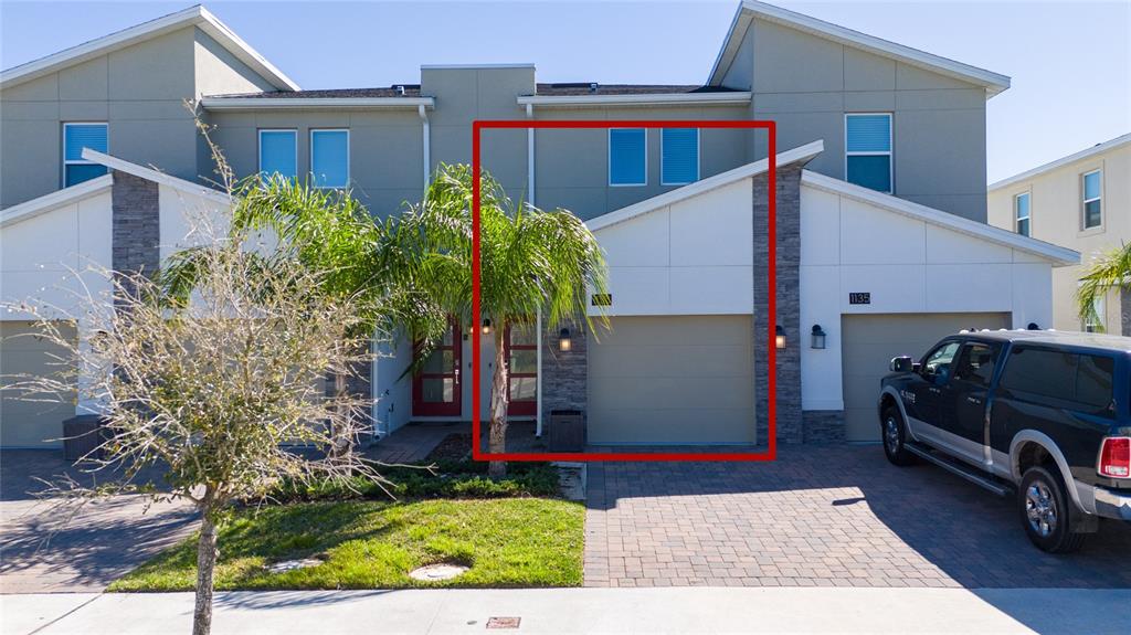 A two-story townhouse exterior features a tan garage, stone accents, and a small palm tree — 1133 CHALLENGE DRIVE UNIT 1133, DAVENPORT, FL