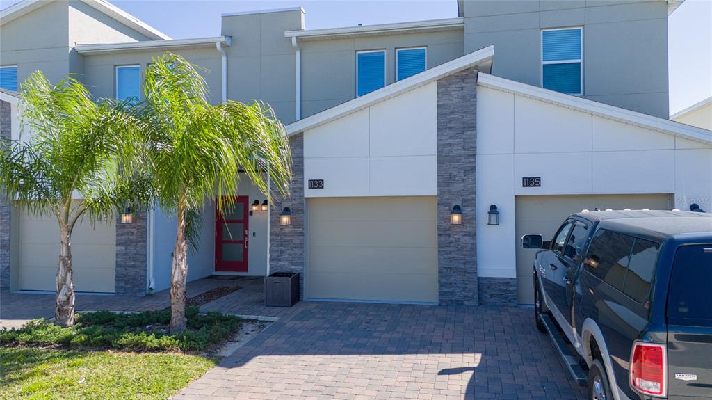 A two-story townhouse exterior features stone accents, a red front door, and paved driveways — 1133 CHALLENGE DRIVE UNIT 1133, DAVENPORT, FL