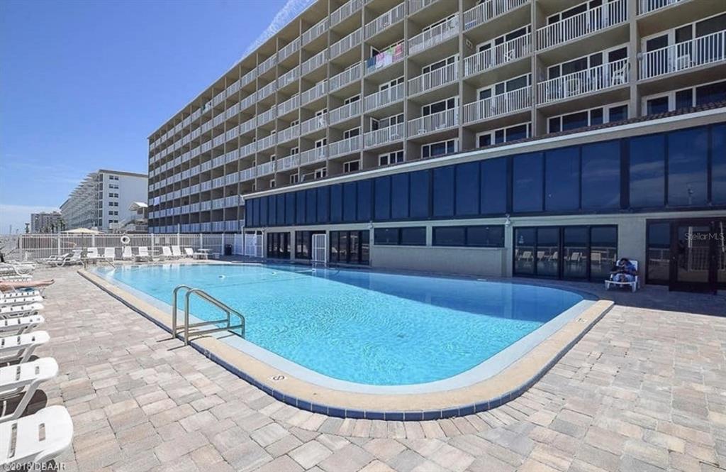 A large rectangular swimming pool sits on a paved patio beside a multi-story hotel building — 3501 S ATLANTIC AVENUE UNIT 3210, DAYTONA BEACH, FL