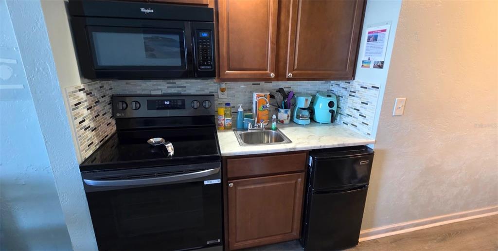 A small kitchen features a black stove, microwave, sink, and mini-fridge with wood cabinets — 3501 S ATLANTIC AVENUE UNIT 3210, DAYTONA BEACH, FL
