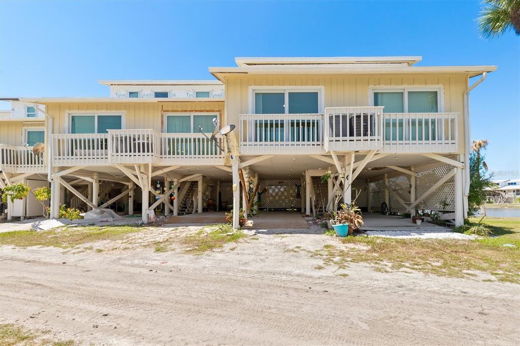 The exterior of a two-story elevated house with wooden decks and a sandy ground level — 9400 LITTLE GASPARILLA ISLAND UNIT G9, BOCA GRANDE, FL