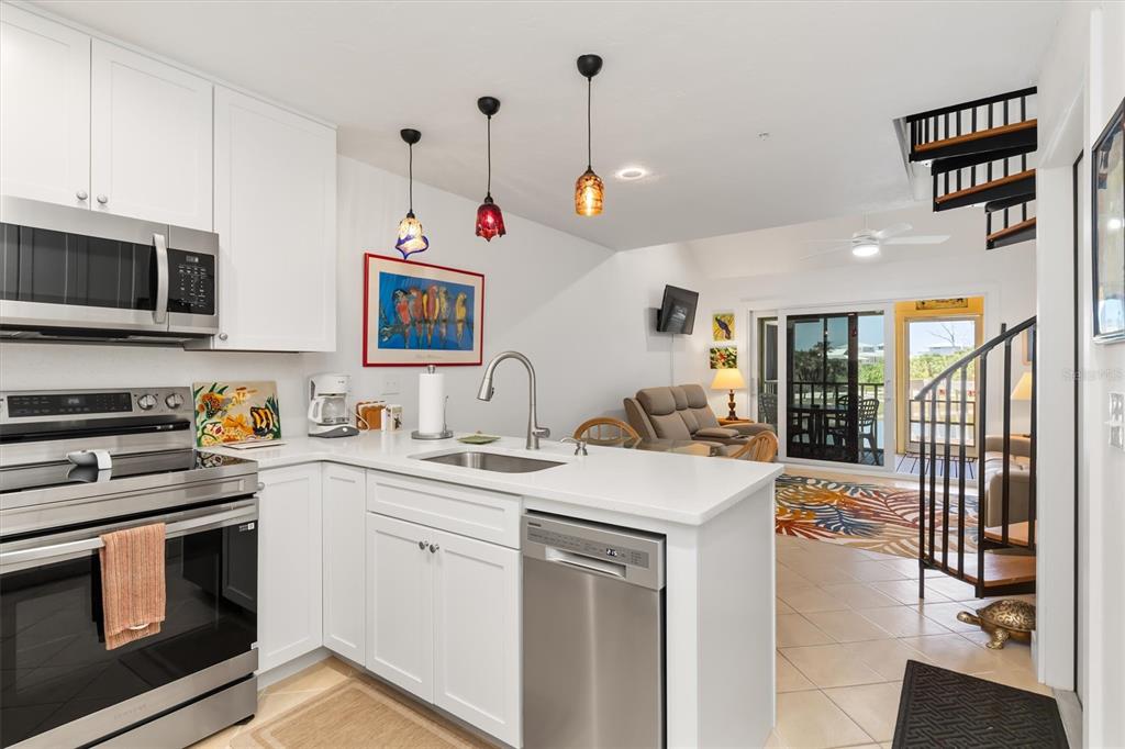 A kitchen with white cabinets and stainless steel appliances overlooks a living area with stairs — 9400 LITTLE GASPARILLA ISLAND UNIT G9, BOCA GRANDE, FL