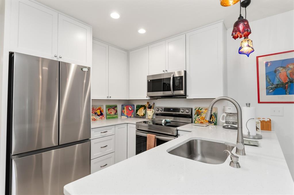 A modern kitchen features white cabinetry, stainless steel appliances, and a white quartz countertop — 9400 LITTLE GASPARILLA ISLAND UNIT G9, BOCA GRANDE, FL