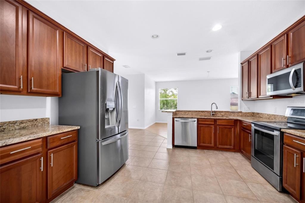 A kitchen features wood cabinets, granite countertops, stainless steel appliances, and tile flooring — 8919 N RIVER ROAD, TAMPA, FL