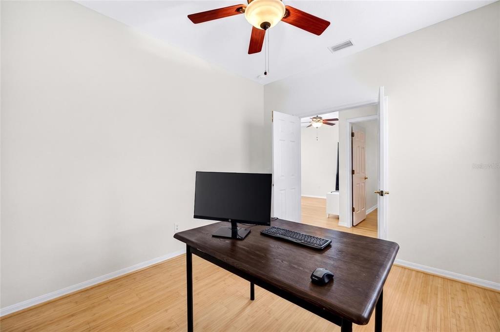 A home office features a dark wood desk, a computer monitor, and light wood flooring — 8919 N RIVER ROAD, TAMPA, FL