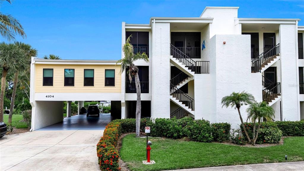 A multi-story apartment building features a covered parking area, exterior staircases, and landscaped grounds — 4104 128TH STREET W UNIT 702, CORTEZ, FL