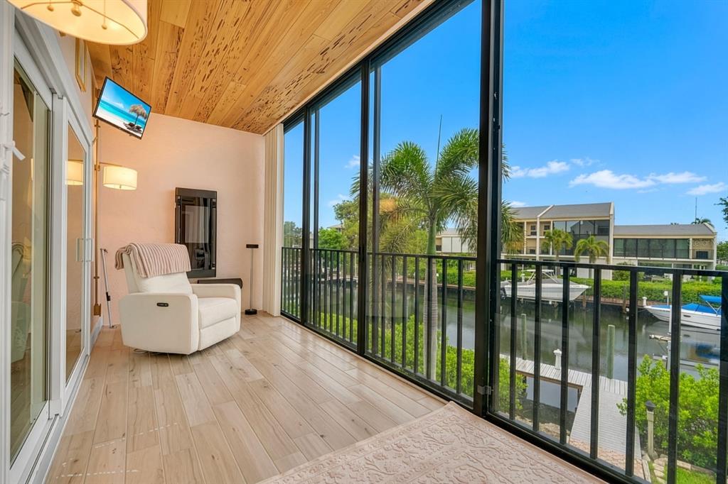 A screened-in balcony with wood-look flooring and a ceiling overlooks a canal with docked boats — 4104 128TH STREET W UNIT 702, CORTEZ, FL