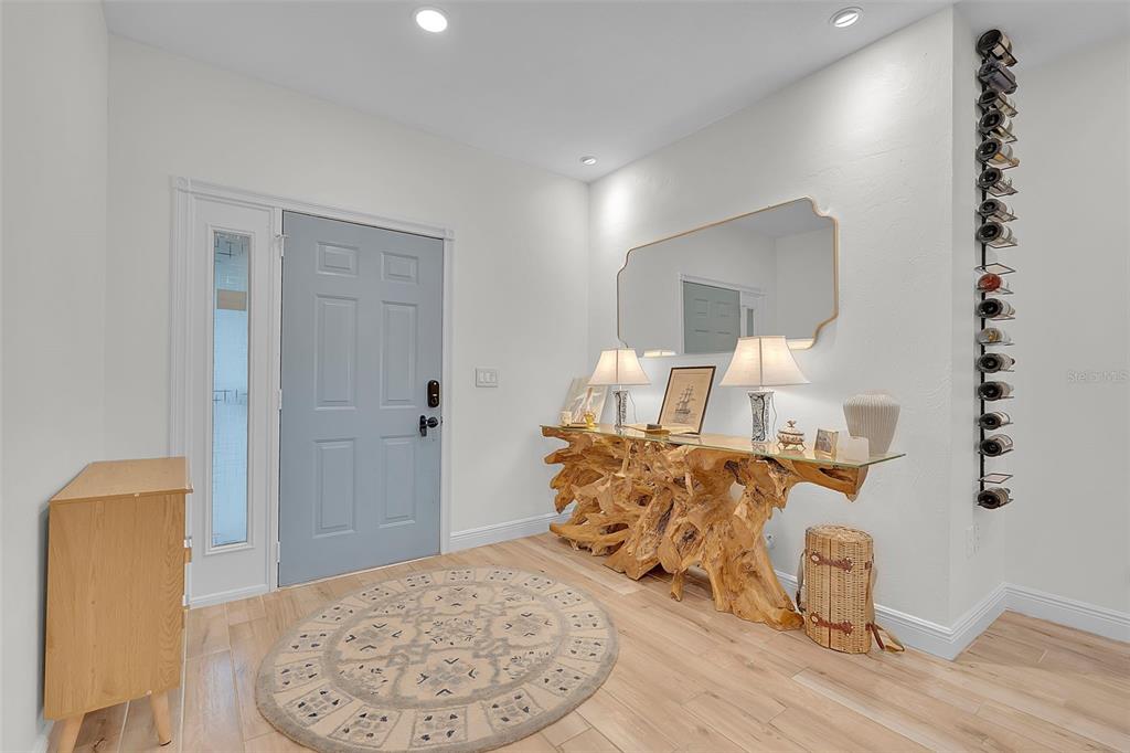 An entryway features a light blue door, a wood-root console table, and a wall-mounted wine rack — 4104 128TH STREET W UNIT 702, CORTEZ, FL