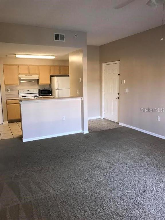 A living room with gray carpeting opens to a kitchen featuring light wood cabinets — 10831 WINDSOR WALK DRIVE UNIT 1308, ORLANDO, FL