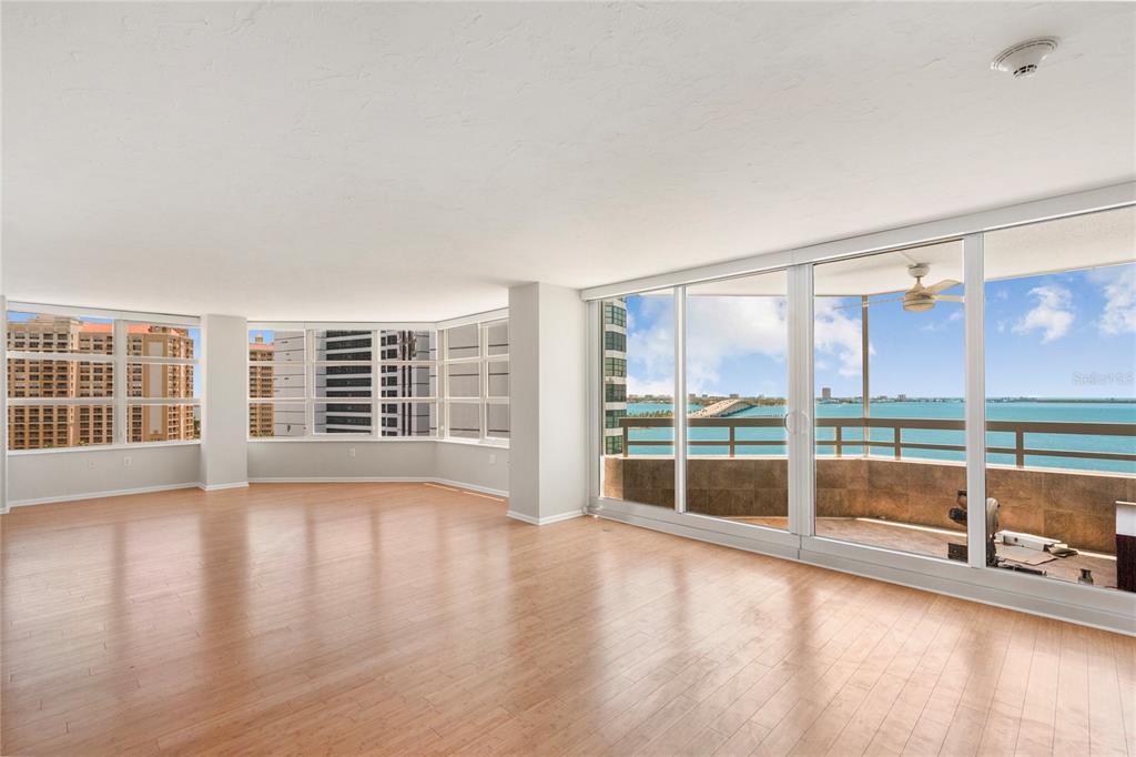 An empty living room with light wood floors, floor-to-ceiling windows, and a balcony overlooking water — 988 BLVD OF THE ARTS UNIT 1209, SARASOTA, FL