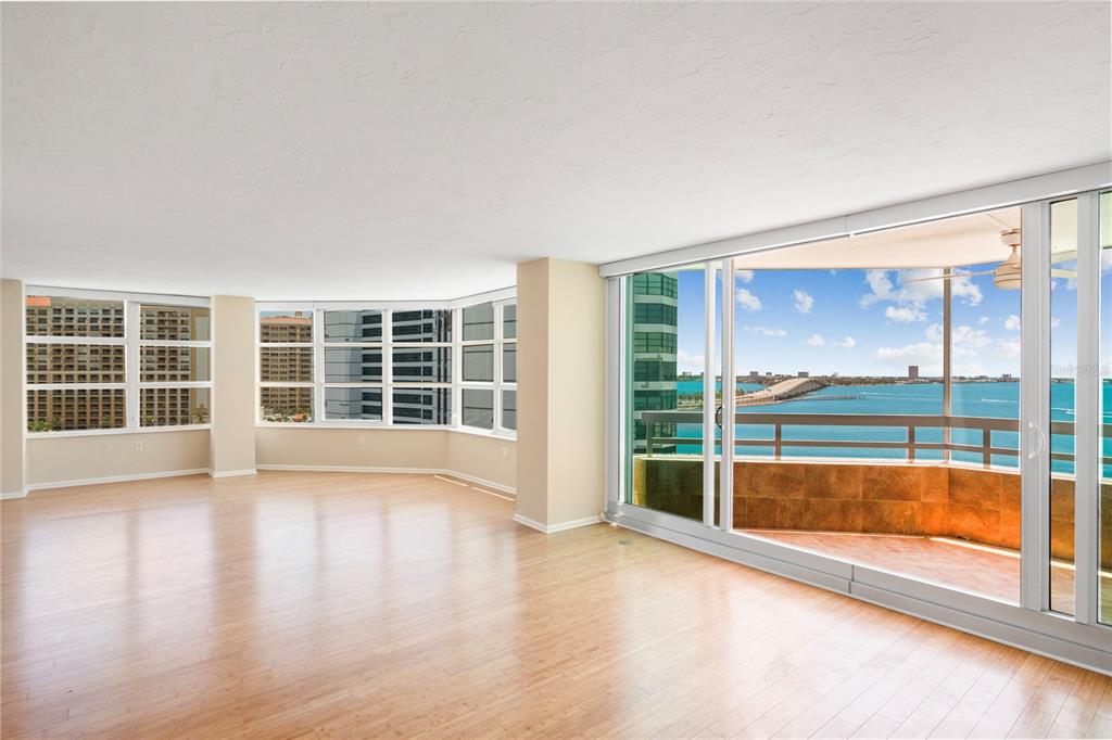 An empty living room with light wood floors, floor-to-ceiling windows, and a balcony overlooking water — 988 BLVD OF THE ARTS UNIT 1209, SARASOTA, FL