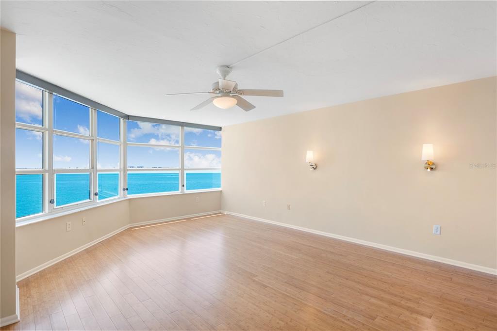 An empty living room features light wood flooring, a ceiling fan, and large windows overlooking water — 988 BLVD OF THE ARTS UNIT 1209, SARASOTA, FL