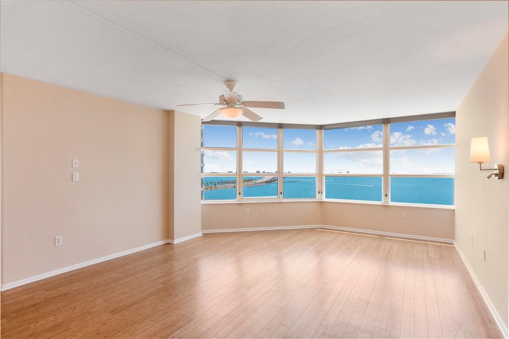 An empty living room with light wood floors, a ceiling fan, and panoramic ocean views — 988 BLVD OF THE ARTS UNIT 1209, SARASOTA, FL