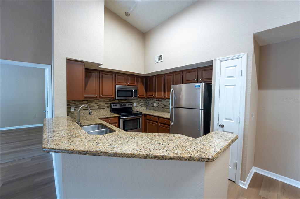 A kitchen features brown cabinets, granite countertops, stainless steel appliances, and a breakfast bar — 13028 PLANTATION PARK CIRCLE UNIT 1225, ORLANDO, FL