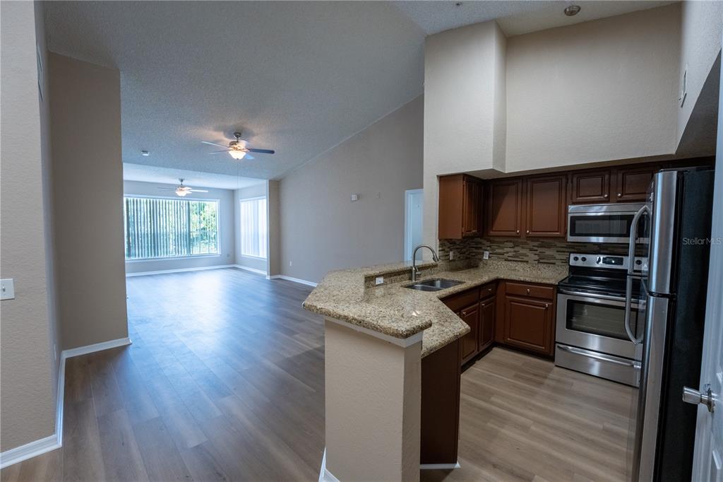 An open-concept kitchen with granite countertops and wood cabinets overlooks a spacious living area — 13028 PLANTATION PARK CIRCLE UNIT 1225, ORLANDO, FL