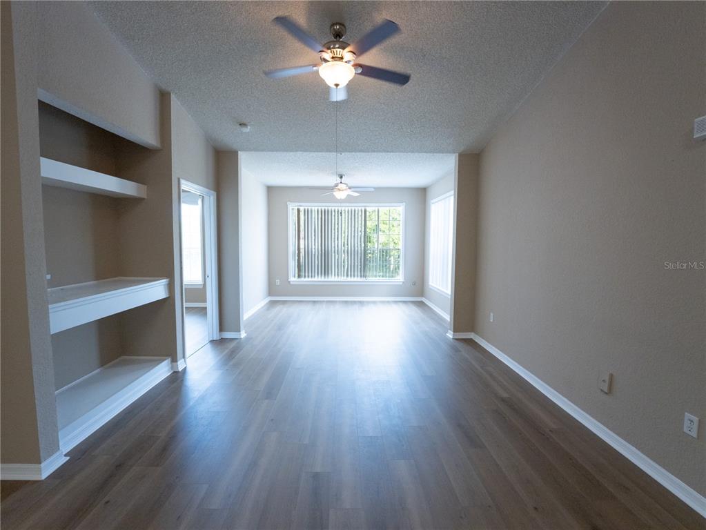 An empty living room features wood-look flooring, two ceiling fans, and built-in wall shelving — 13028 PLANTATION PARK CIRCLE UNIT 1225, ORLANDO, FL