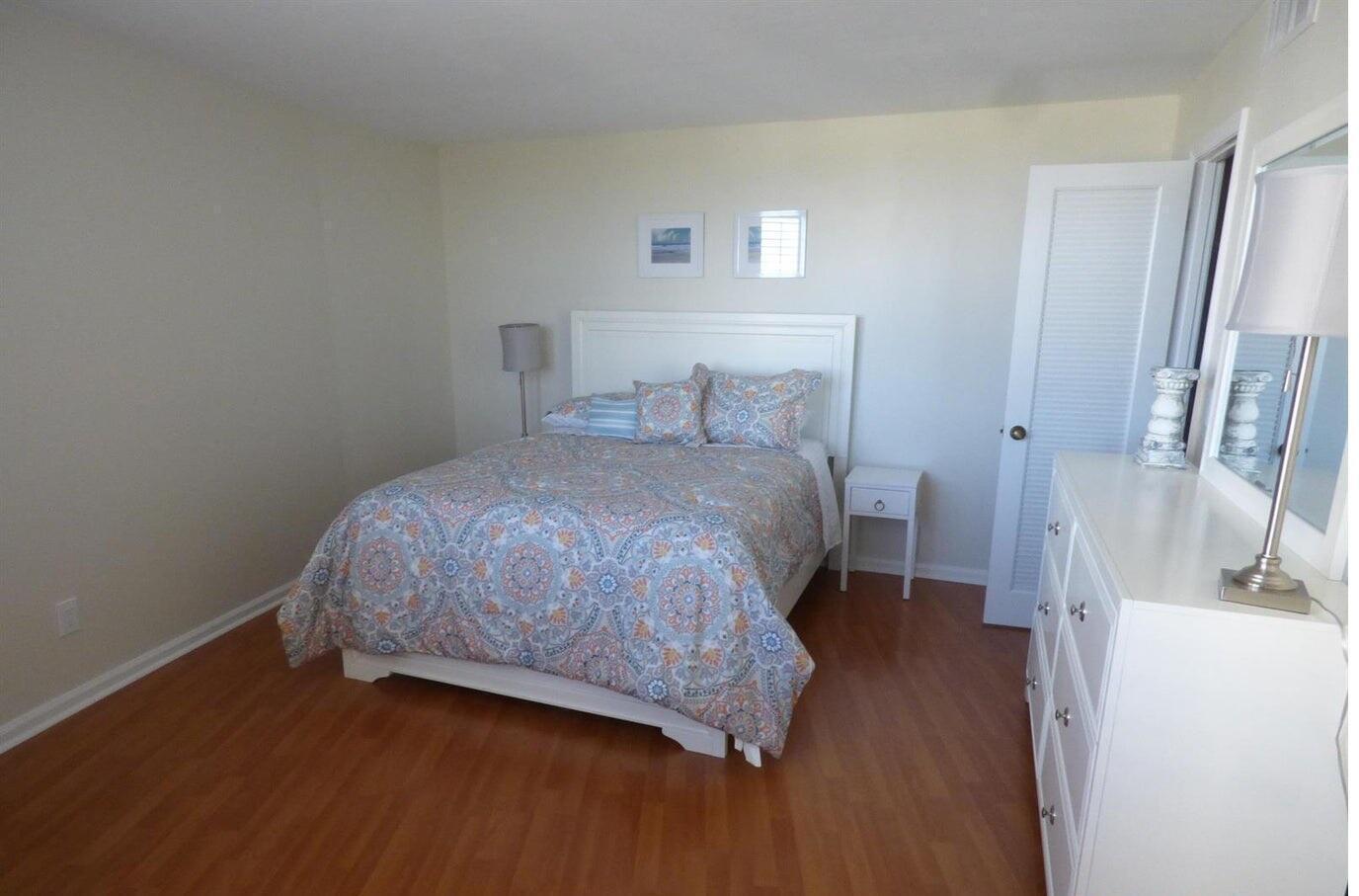 A bedroom with a white bed frame, patterned bedding, wood flooring, and a white dresser — 2800 N Ocean Drive # 5c, Singer Island FL 33404, SINGER ISLAND, FL