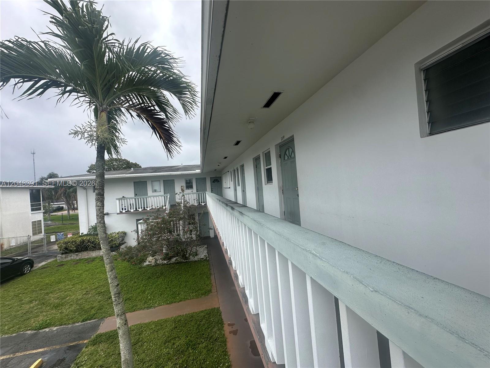 An exterior view shows a second-story walkway with white railings overlooking a grassy courtyard — 6740 Arbor Dr # 204, Miramar FL 33023, MIRAMAR, FL