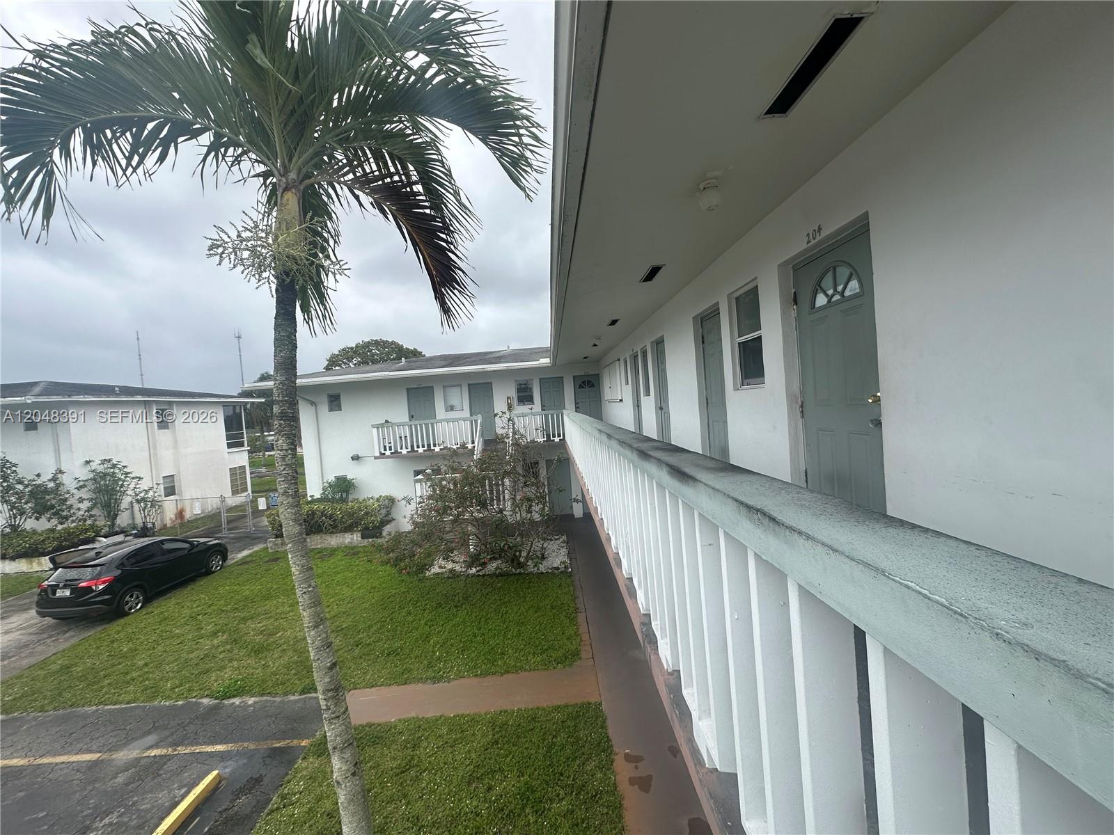 An exterior view shows a second-story walkway with white railings overlooking a grassy courtyard — 6740 Arbor Dr # 204, Miramar FL 33023, MIRAMAR, FL
