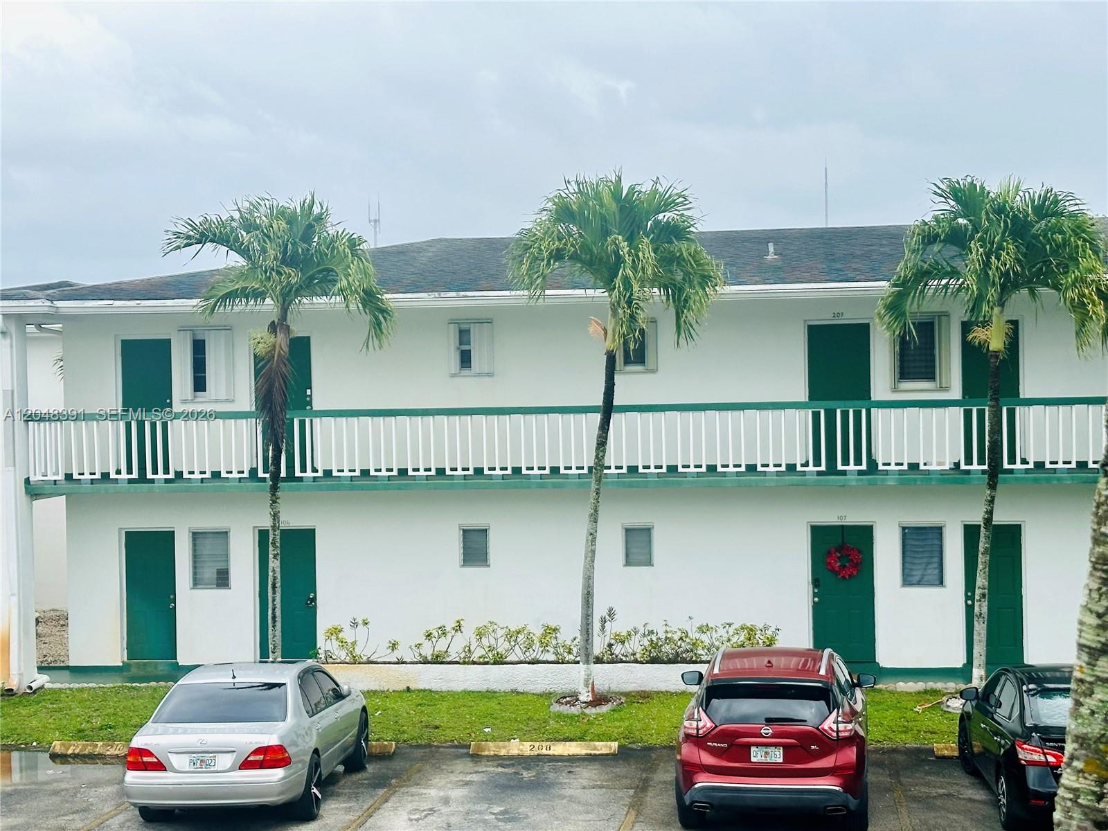 A two-story white apartment building with green doors and a balcony sits above a parking lot — 6740 Arbor Dr # 204, Miramar FL 33023, MIRAMAR, FL