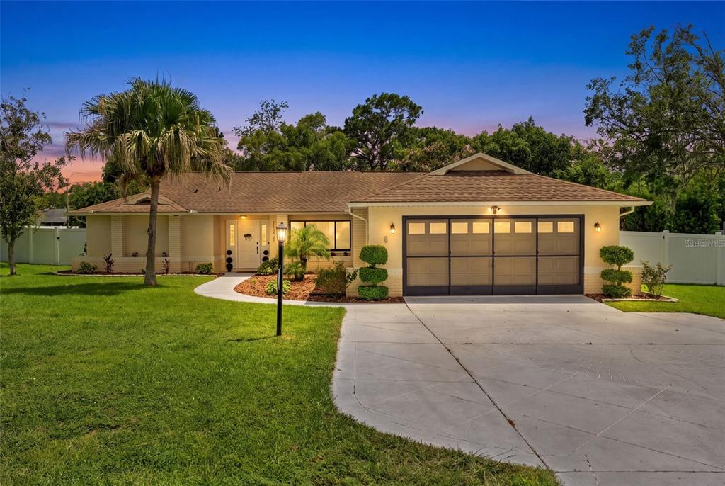 A single-story house with a tan exterior, a two-car garage, and a palm tree — 11201 RAINBOW WOODS LOOP, SPRING HILL, FL