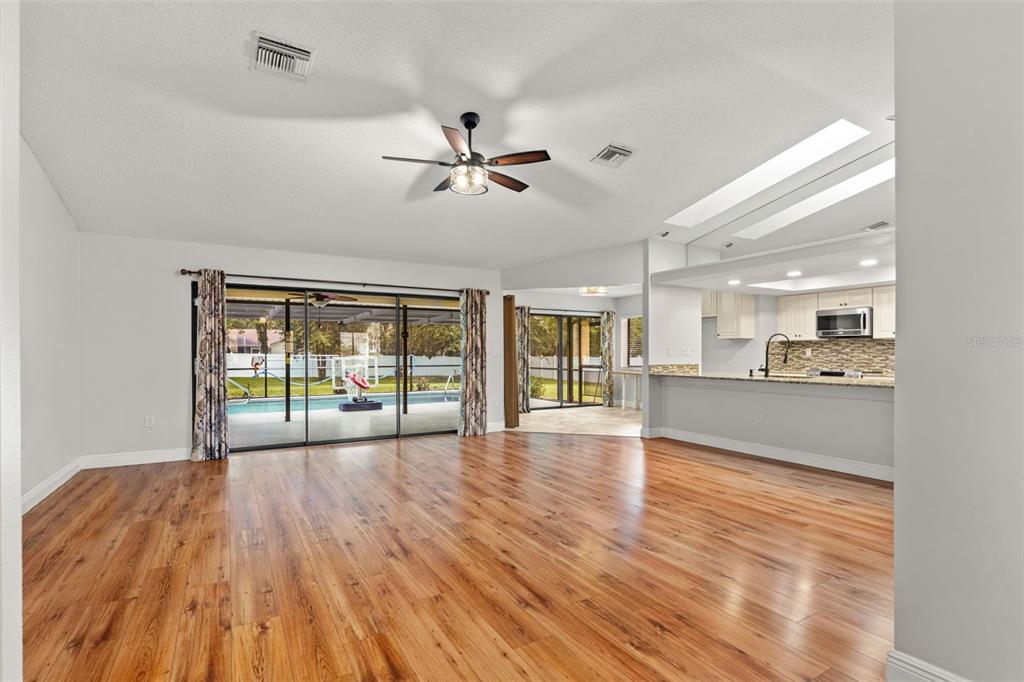 A living room with wood-look flooring, a ceiling fan, and a view of a pool — 11201 RAINBOW WOODS LOOP, SPRING HILL, FL
