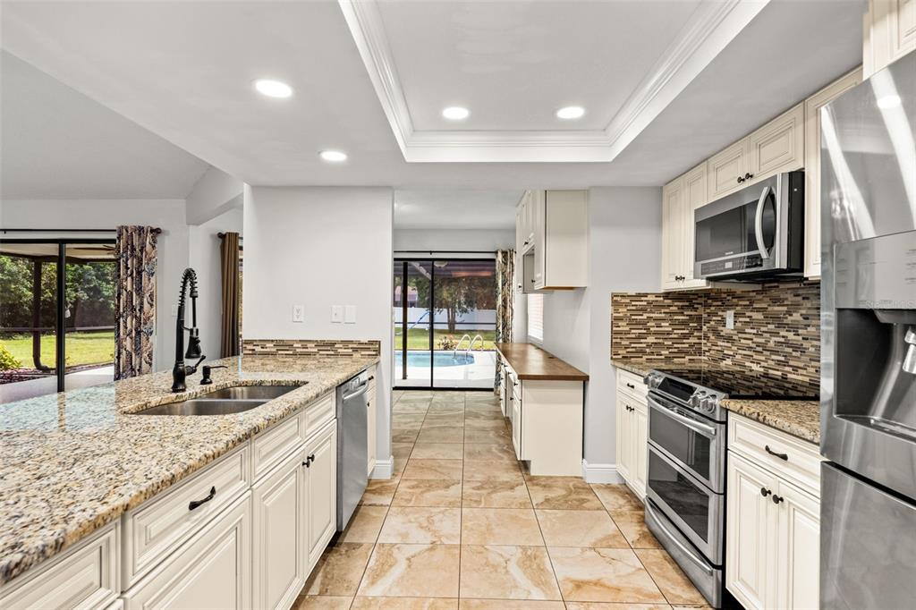 A kitchen features white cabinets, granite countertops, stainless steel appliances, and a view of a pool — 11201 RAINBOW WOODS LOOP, SPRING HILL, FL
