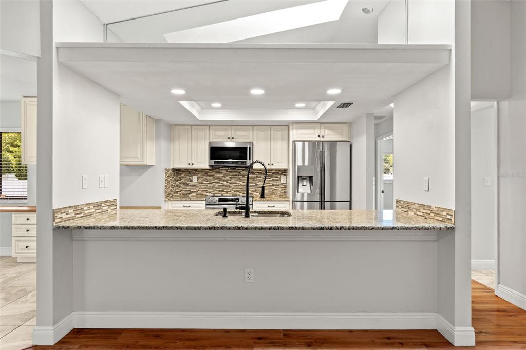 A kitchen features white cabinets, granite countertops, a tiled backsplash, and stainless steel appliances — 11201 RAINBOW WOODS LOOP, SPRING HILL, FL