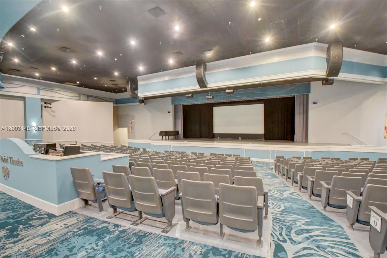 An indoor theater features rows of gray seats facing a stage with a projection screen — 150 Tuscany C # 150, Delray Beach FL 33446, DELRAY BEACH, FL