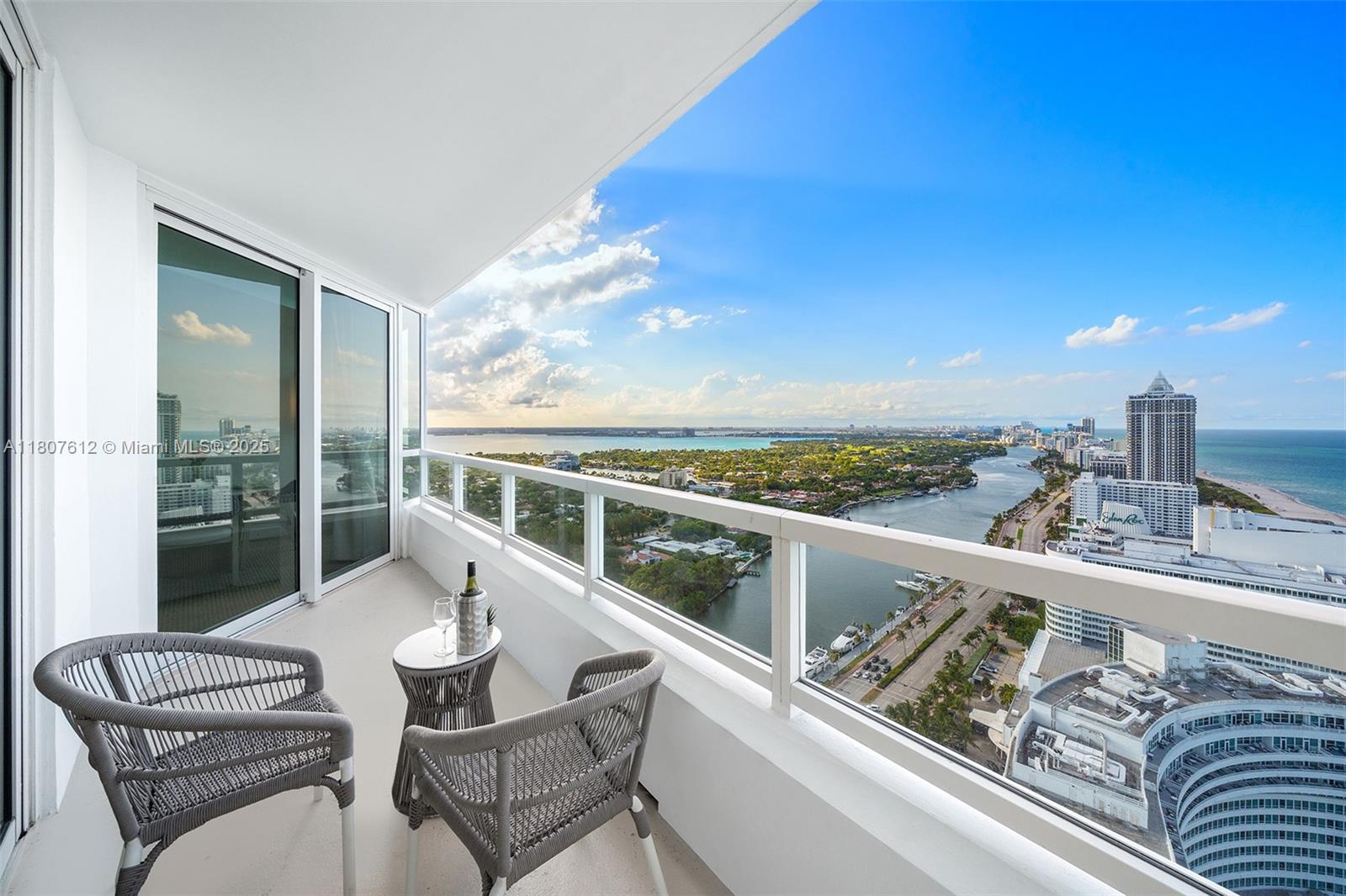 A balcony with two chairs and a small table overlooks a coastal city and ocean — 4401 Collins Ave # 3505, Miami Beach FL 33140, MIAMI BEACH, FL