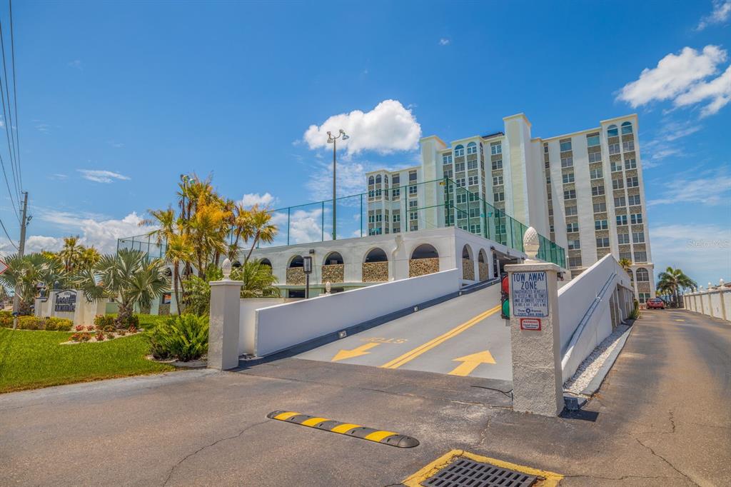 A concrete ramp leads to a parking garage beside a tall, multi-story residential building — 4950 GULF BOULEVARD UNIT 404, ST PETE BEACH, FL