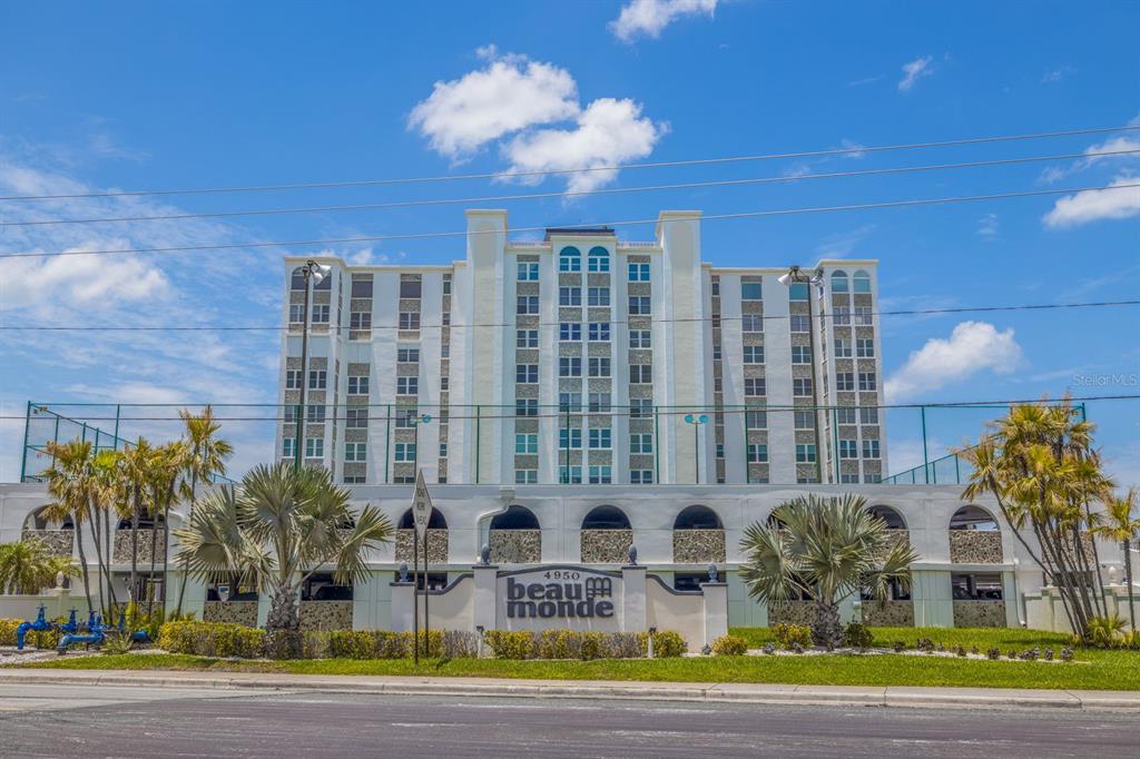 A multi-story white apartment building stands behind a low wall with palm trees — 4950 GULF BOULEVARD UNIT 404, ST PETE BEACH, FL